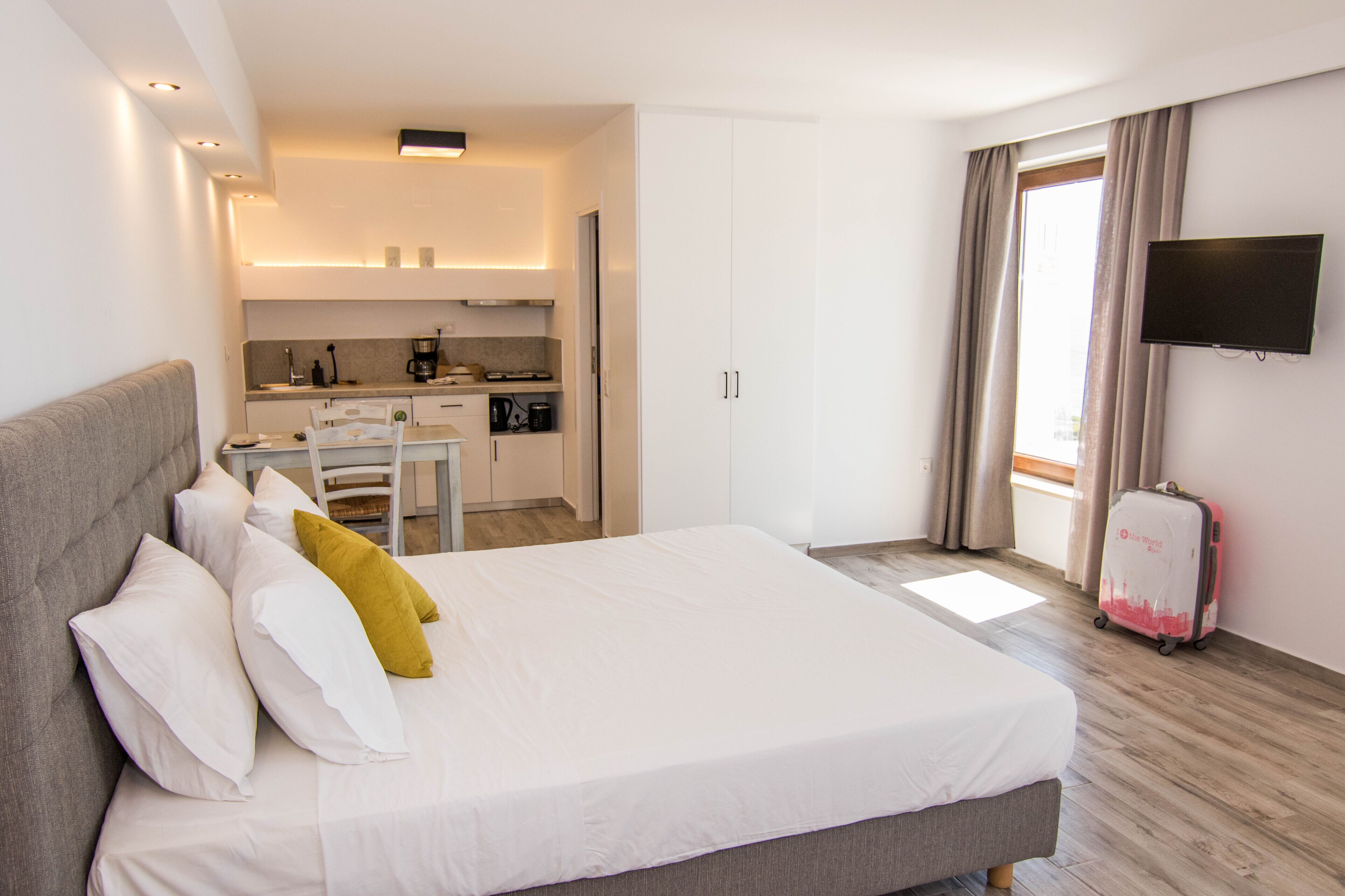 A hotel room with a bed, a kitchenette, a TV, and a suitcase.