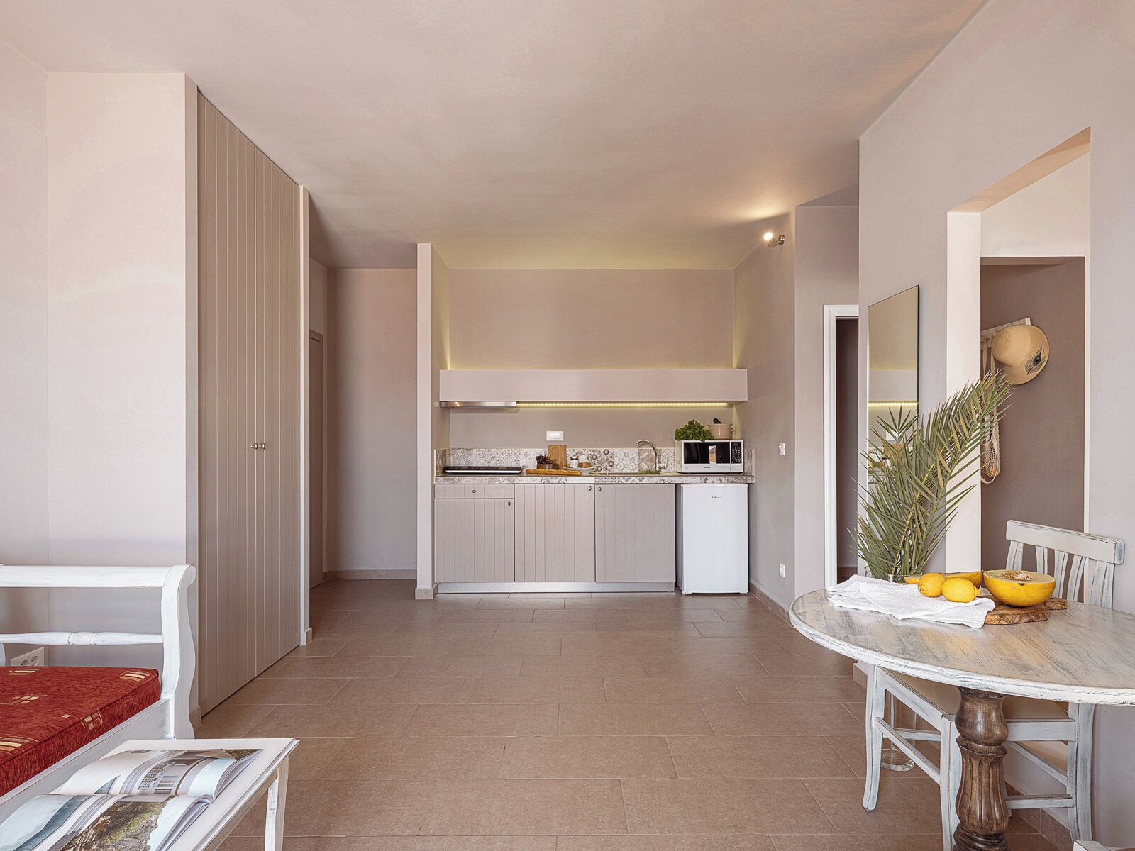 A compact kitchen with a microwave, sink, and cabinets. There is a dining table with chairs and a small plant.
