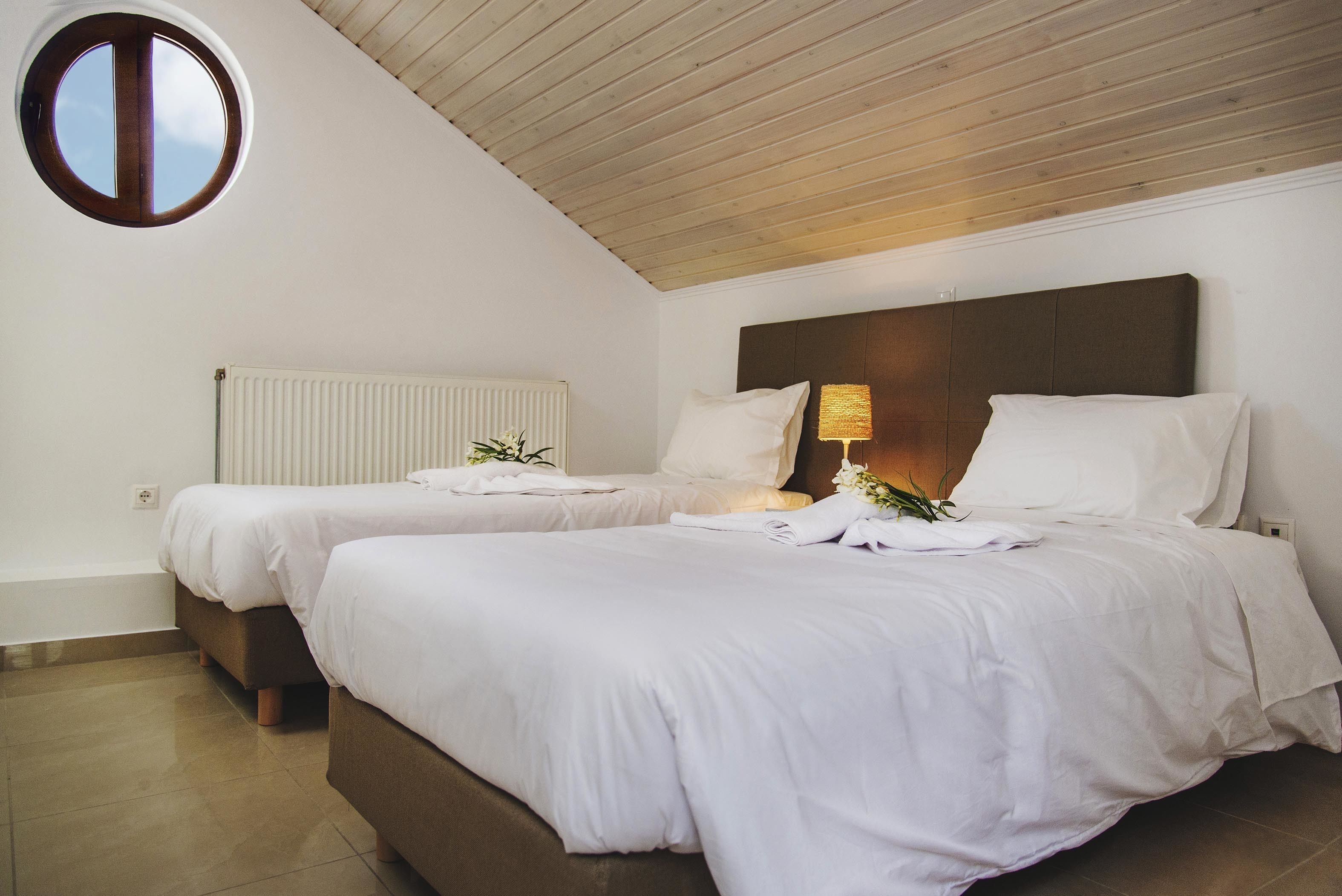 A hotel room with two beds, a wooden ceiling, a radiator, and a small window.
