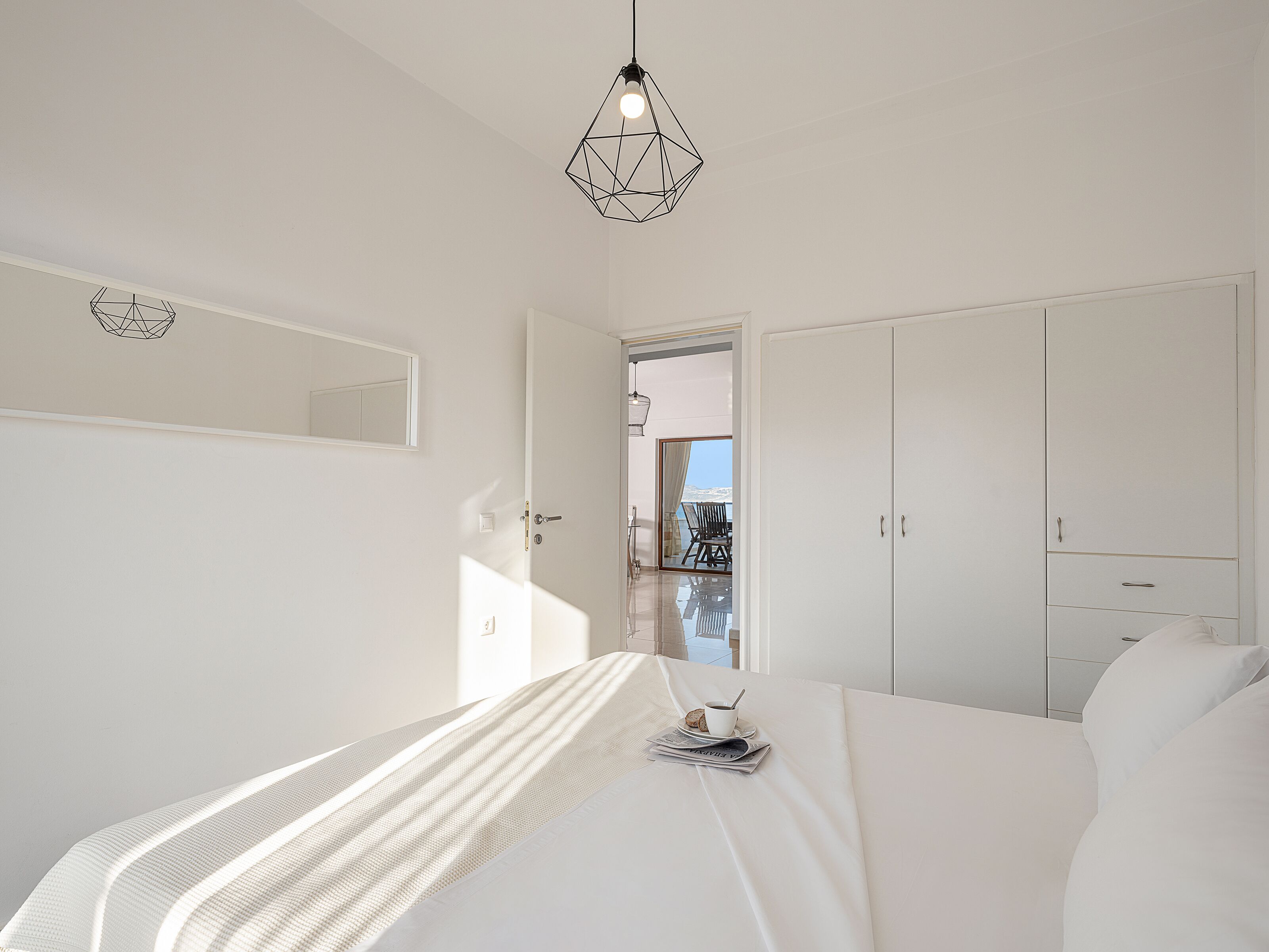 Ein modernes Schlafzimmer mit einem Bett, einem Kleiderschrank und einer geometrischen Pendelleuchte.