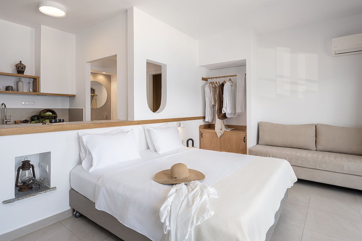 Moderni hotellihuone, jossa on sänky, puinen pääty, peilillä varustettu meikkipöytä, vaateteline ja sohva.