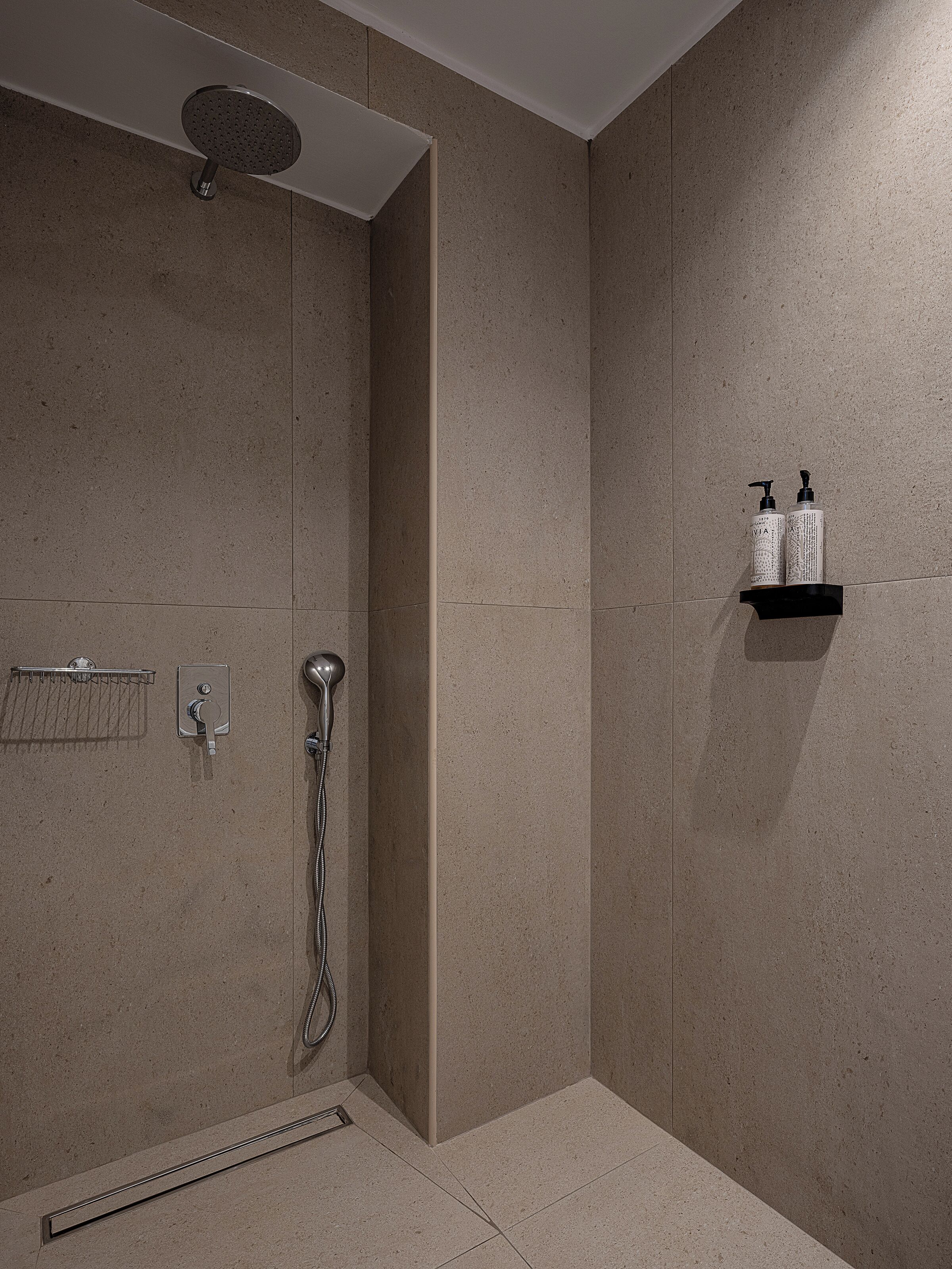 Un espace douche moderne doté d’un pommeau de douche à main, d’un robinet mural et d’une étagère contenant deux bouteilles de shampoing.