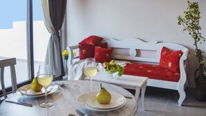 Una mesa de comedor con platos de peras y copas de vino blanco, un sofá blanco con cojines rojos y una planta en maceta en una esquina.