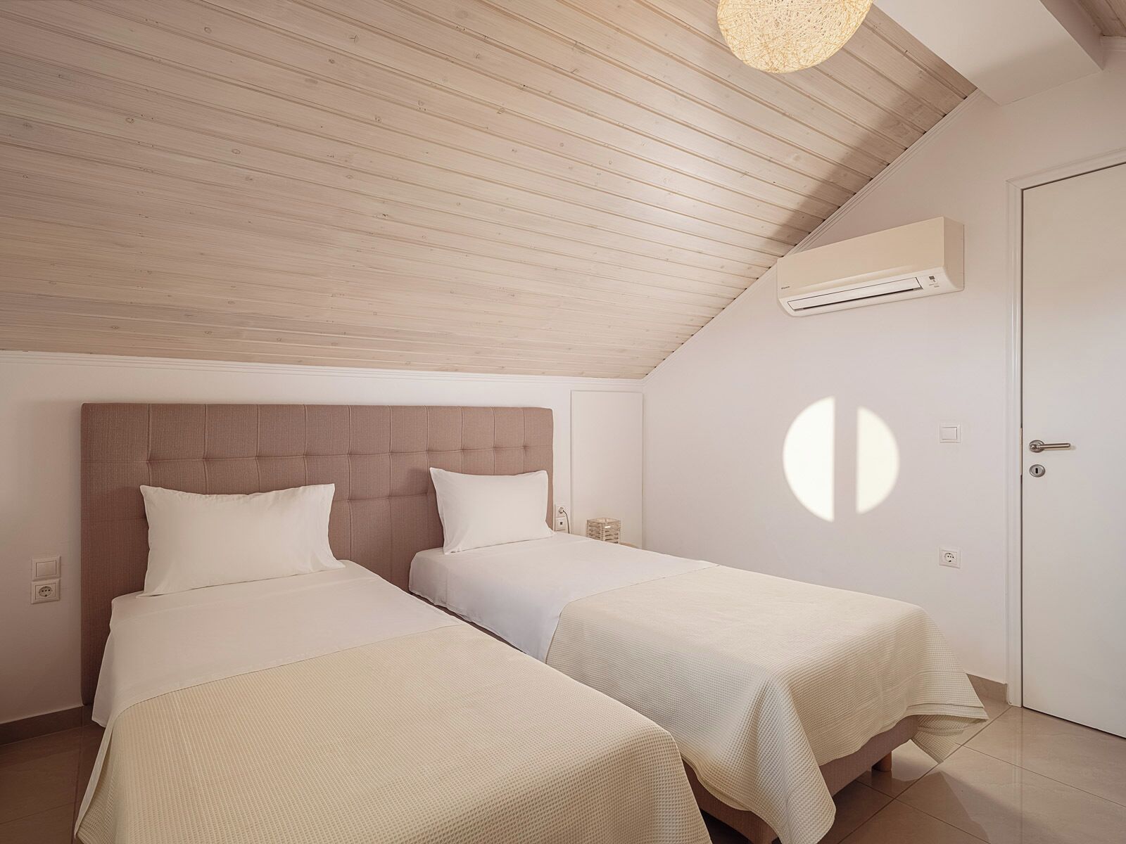 A bedroom with two beds, a wooden ceiling, and a door with a circular window.