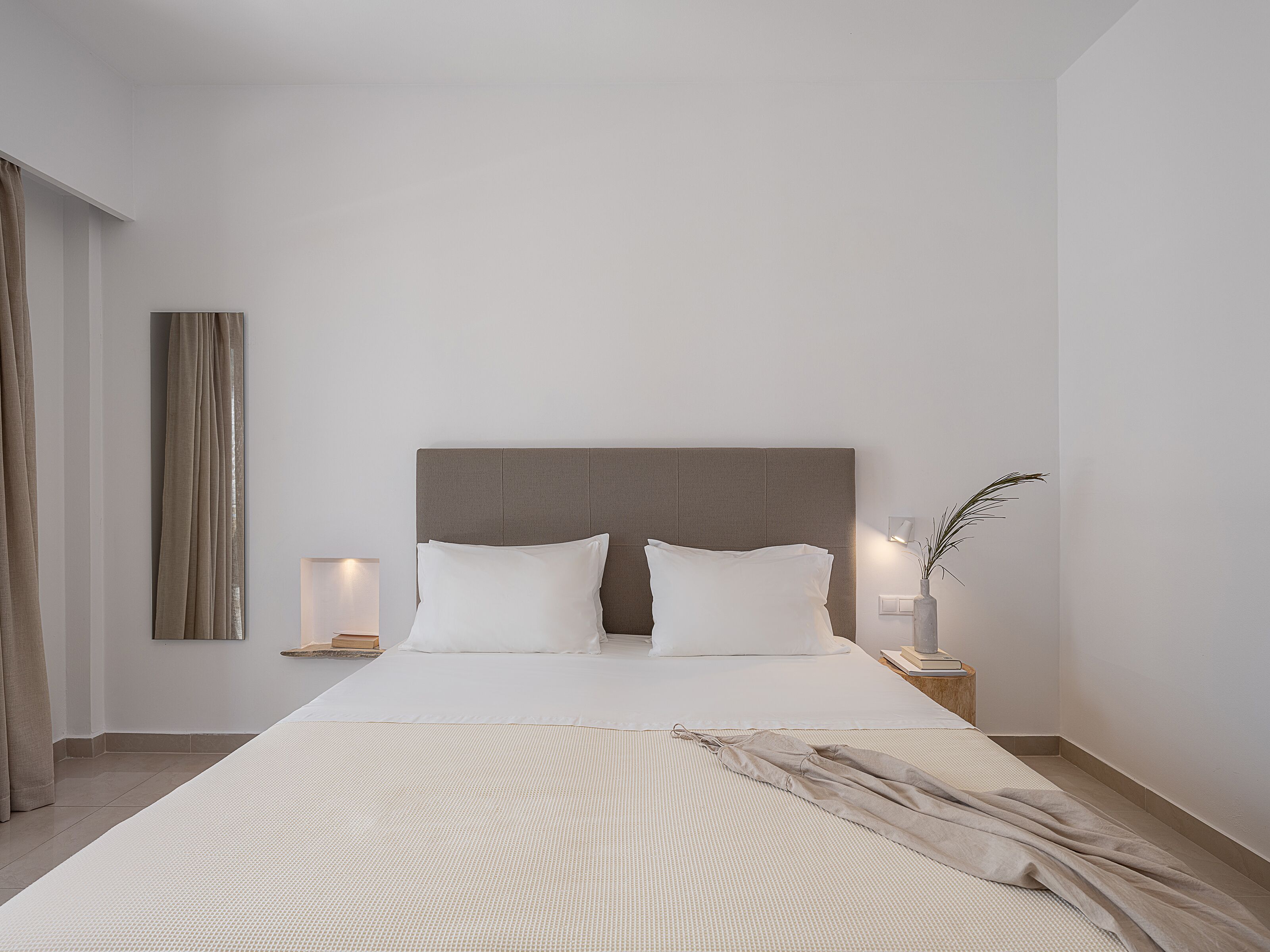 A modern bedroom with a large bed, a bedside table with a lamp, and a nightstand with a vase.