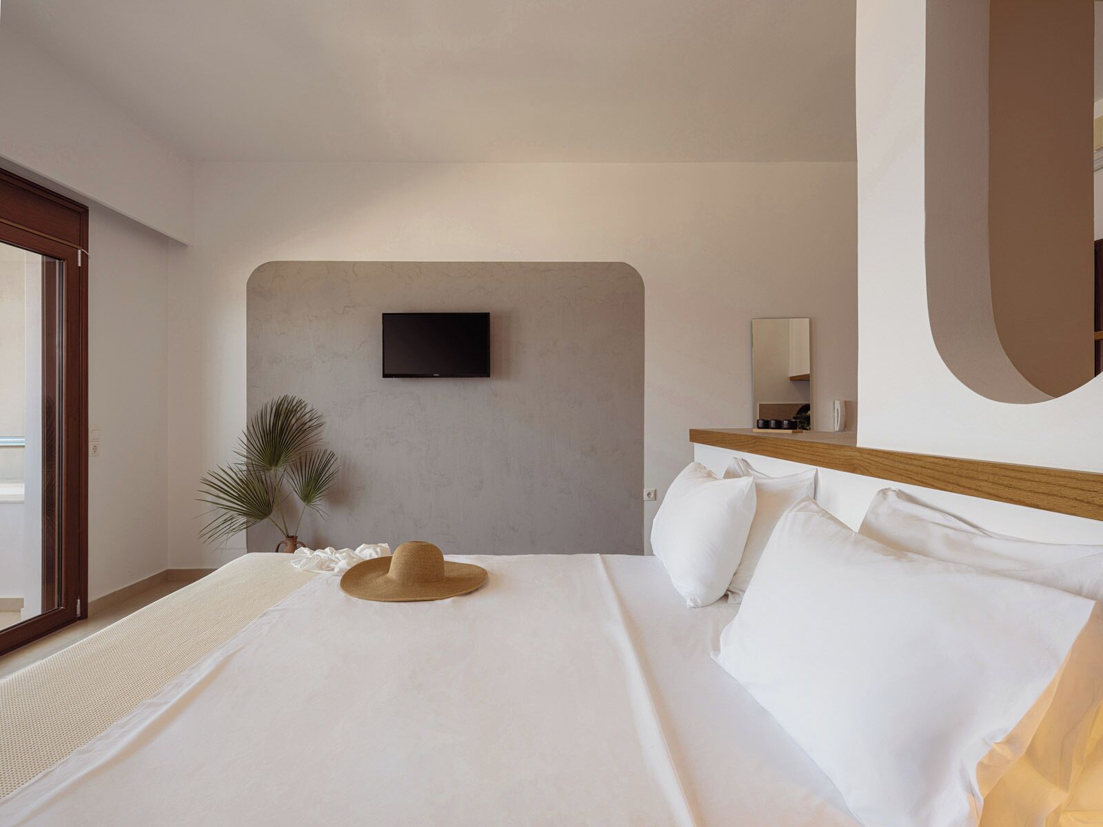 A bedroom with a bed, a television mounted on the wall, a mirror, and a potted plant.