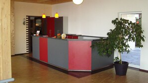 En modern receptionsdisk med en krukväxt, synliga träbjälkar i taket och utsikt över omgivningen.