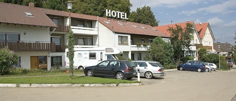 Un hôtel avec une enseigne indiquant « HÔTEL », un fourgon blanc et plusieurs voitures garées devant.