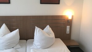 Ett hotellrum med två sängar, där varje säng har vita sängkläder och kuddar, ett träfärgat sänggavel och två tavlor på väggen.