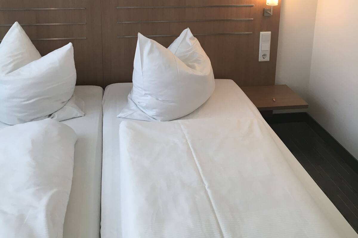 A hotel room with two beds, each with white bedding and pillows, a wooden headboard, and two paintings on the wall.