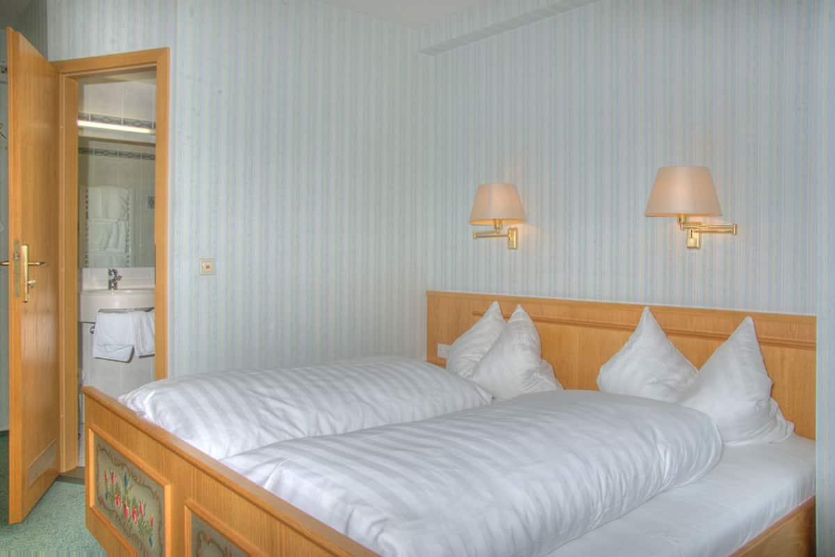 A bedroom with two single beds, a wooden headboard, a wall-mounted lamp, and a bathroom visible through an open door.