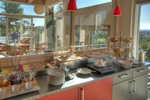 Disposición de bufé con diferentes alimentos y condimentos, una balanza y vistas al exterior a través de amplias ventanas.