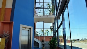 A modern building with a blue and orange facade, a glass elevator, and a balcony with potted plants. - Hotel Los Barruecos (Malpartida de Caceres)