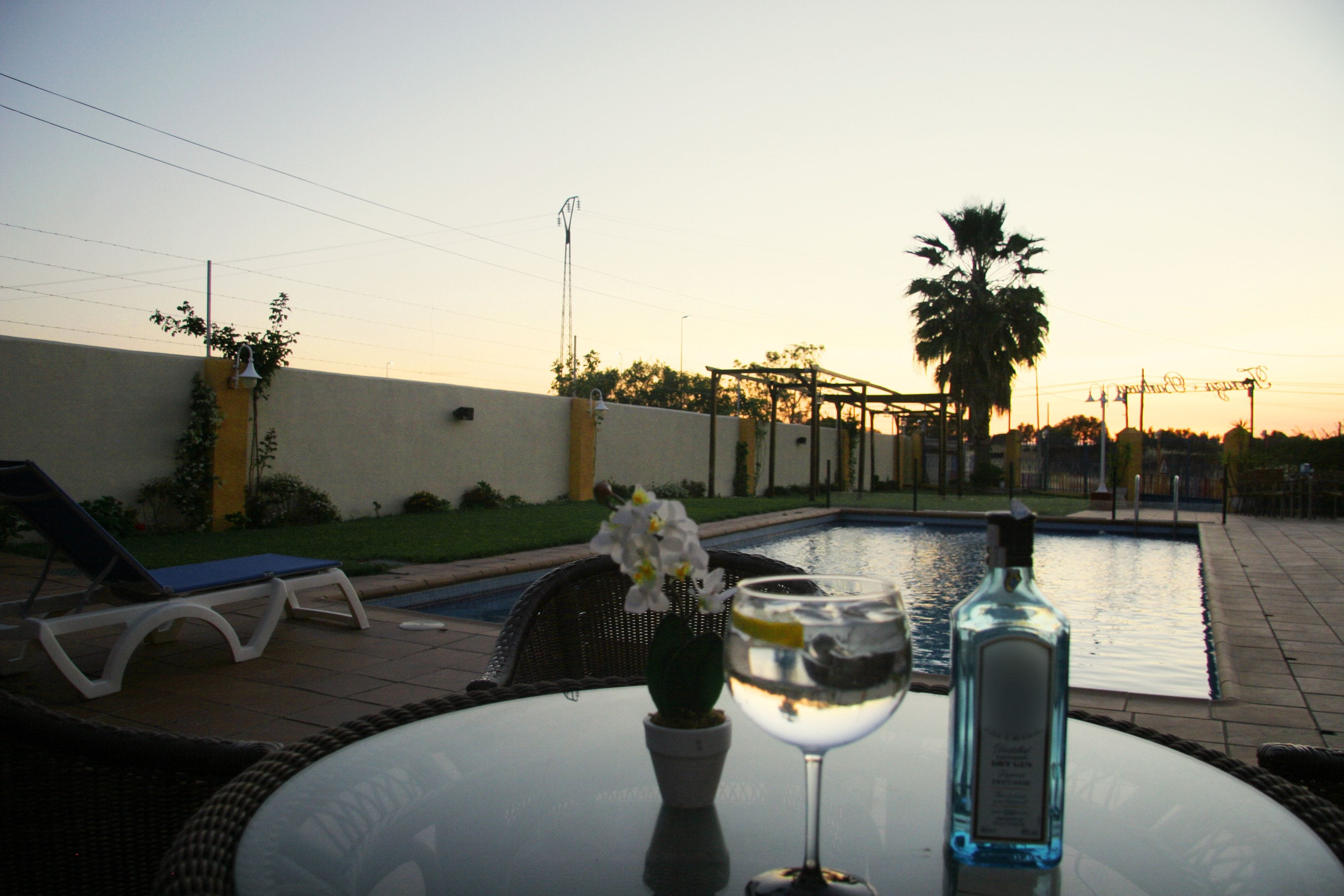 Escena junto a la piscina con una mesa de vidrio, una botella y un vaso de agua.