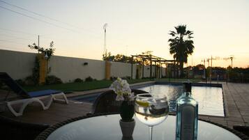 Escena junto a la piscina con una mesa de vidrio, una botella y un vaso de agua.