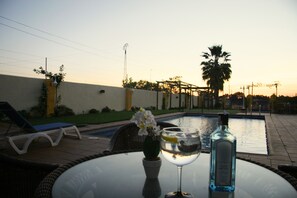 A poolside setting with a glass table, a bottle, and a glass of water. - Hotel Los Barruecos (Malpartida de Caceres)