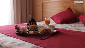 Una bandeja de desayuno ordenada sobre la cama, con una colcha estampada con flores, cabecera de madera y almohada roja.