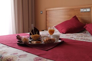A neatly arranged breakfast tray on a bed with a floral bedspread, a wooden headboard, and a red pillow. - Hotel Los Barruecos (Malpartida de Caceres)