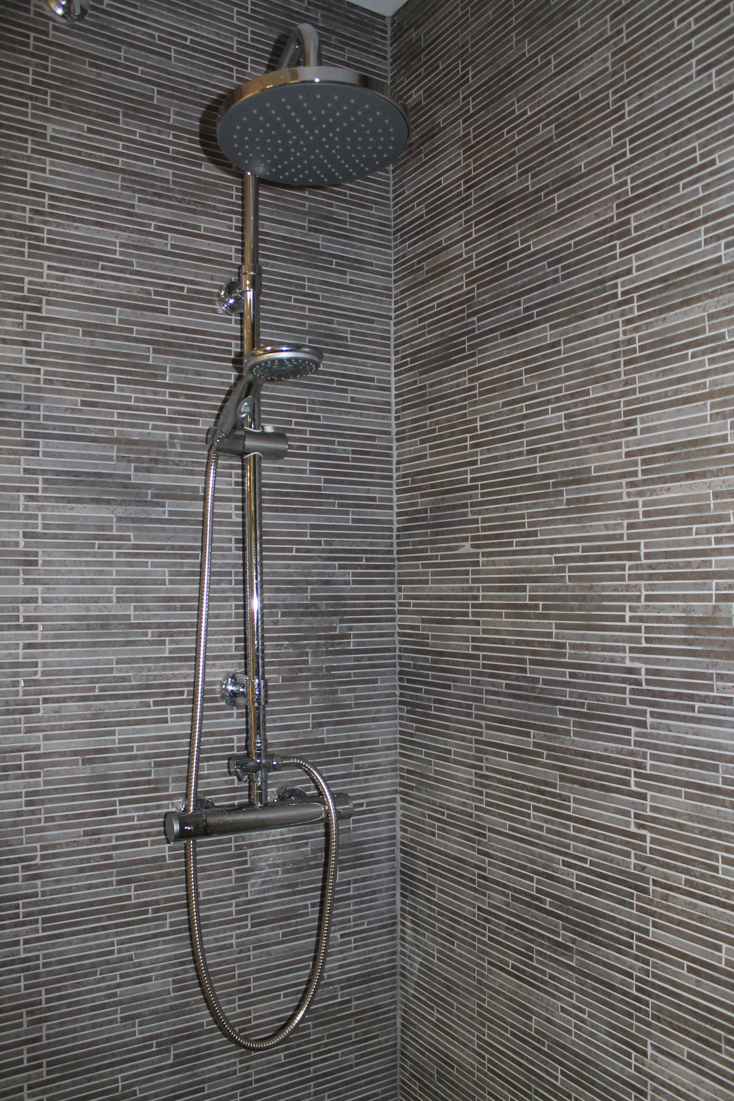 A shower with a rain showerhead and a handheld showerhead mounted on a wall with a brick pattern.