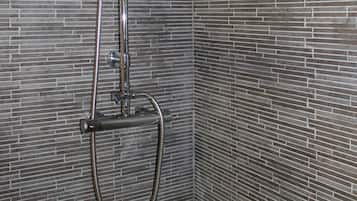 A shower with a rain showerhead and a handheld showerhead mounted on a wall with a brick pattern.
