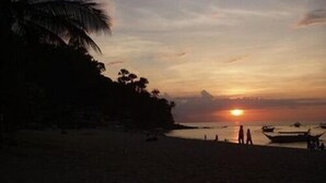 Ein Strand bei Sonnenuntergang mit Silhouetten von Menschen und Booten.