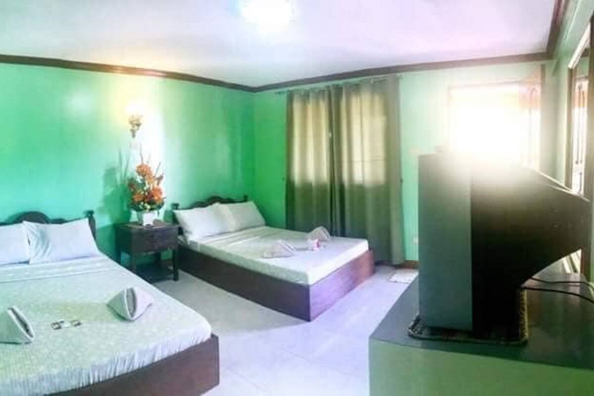 A hotel room with two beds, a desk, a TV, and a window with curtains.