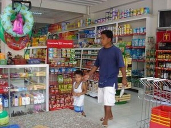 A store interior with shelves stocked with various products, a child and an adult present, and a display counter with items.