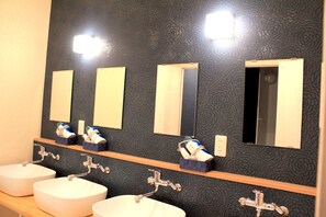 Un baño con tres lavamanos, un espejo y una repisa con artículos de aseo.