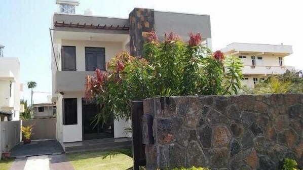 A modern two-story house with a stone wall in the foreground and a well-maintained garden. - Happy Villa (Trou aux Biches)