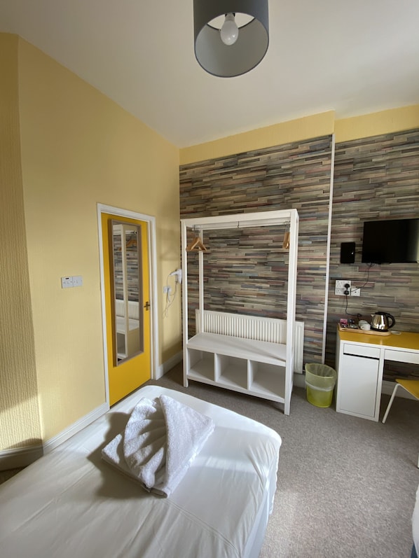 A hotel room with a bed, a desk, a bench, a TV, and a wall with a wood-like pattern. - WiseStay (Cardiff)