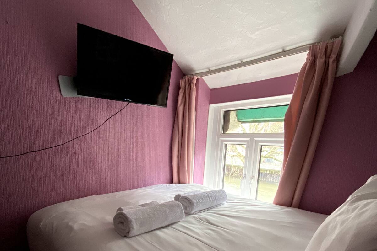 Une chambre d’hôtel avec un lit, un téléviseur à écran plat fixé au mur et une fenêtre avec des rideaux.