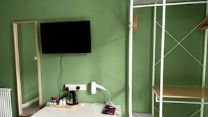 A room with a green wall, a white desk, a yellow chair, a TV mounted on the wall, and a white radiator. - WiseStay (Cardiff)