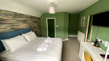 A hotel room with a bed, a desk, and a green accent wall.