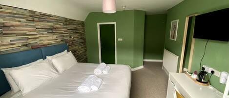 Quarto de hotel com cama, escrivaninha e uma parede verde.