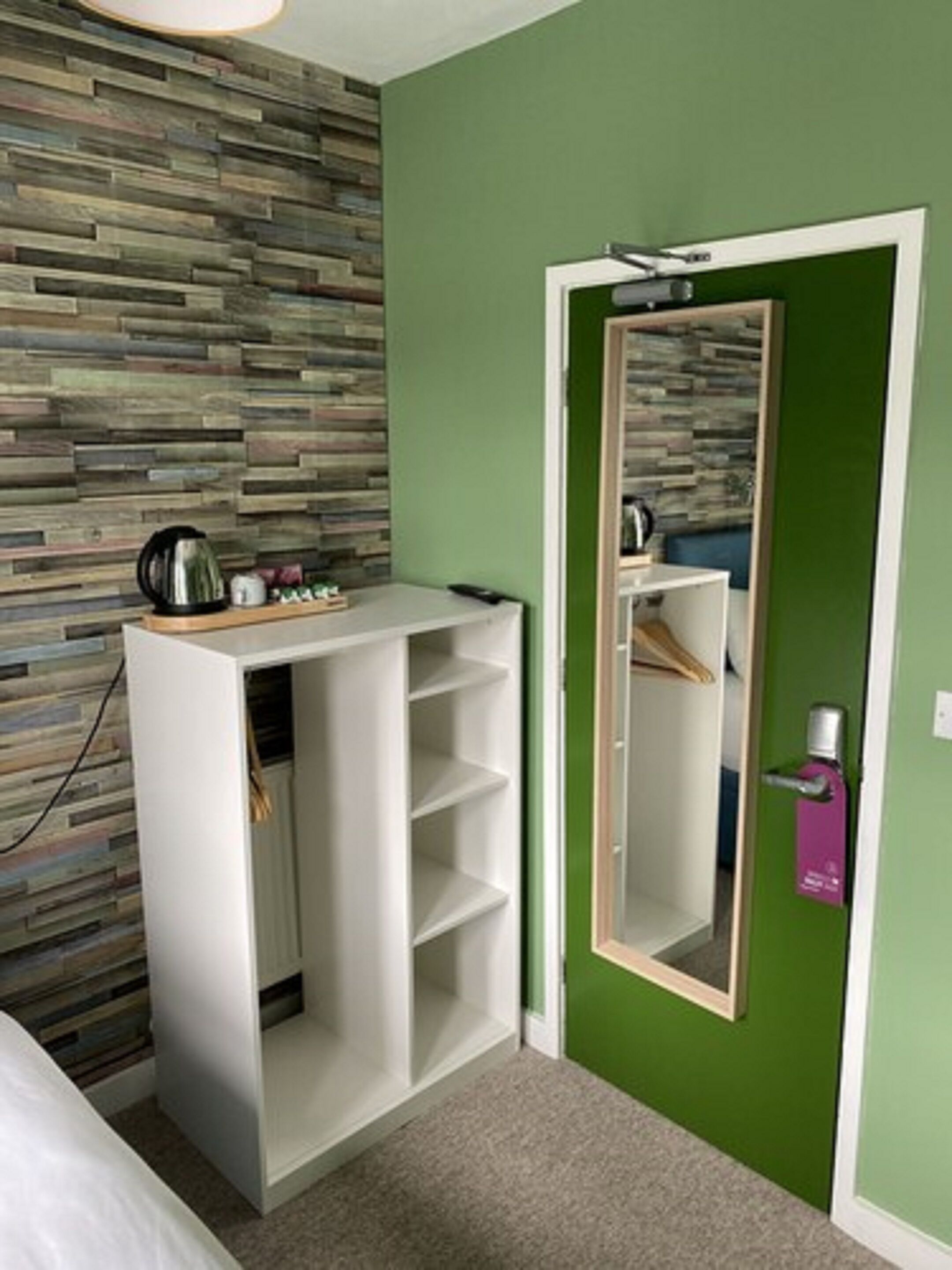 Un dormitorio con pared verde, pared de listones de madera, armario blanco, espejo y puerta con cerradura.