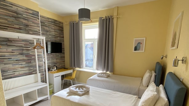A hotel room with a bunk bed, a desk, a chair, a small round table, and a window with curtains. - WiseStay (Cardiff)