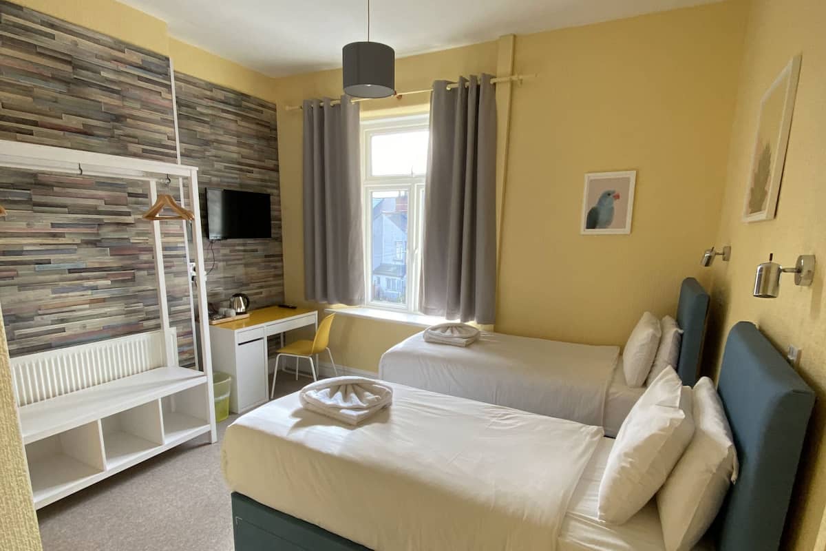 Une chambre d’hôtel avec un lit superposé, un bureau, une chaise, une petite table ronde et une fenêtre avec des rideaux.