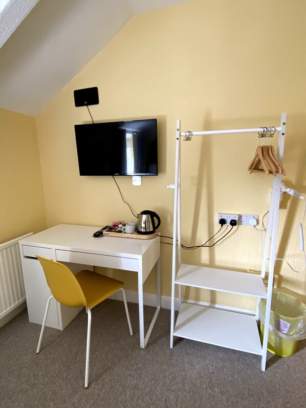A room with a white desk, a yellow chair, a mounted TV, a radiator, a shelf with a kettle, and a clothes drying rack. - WiseStay (Cardiff)