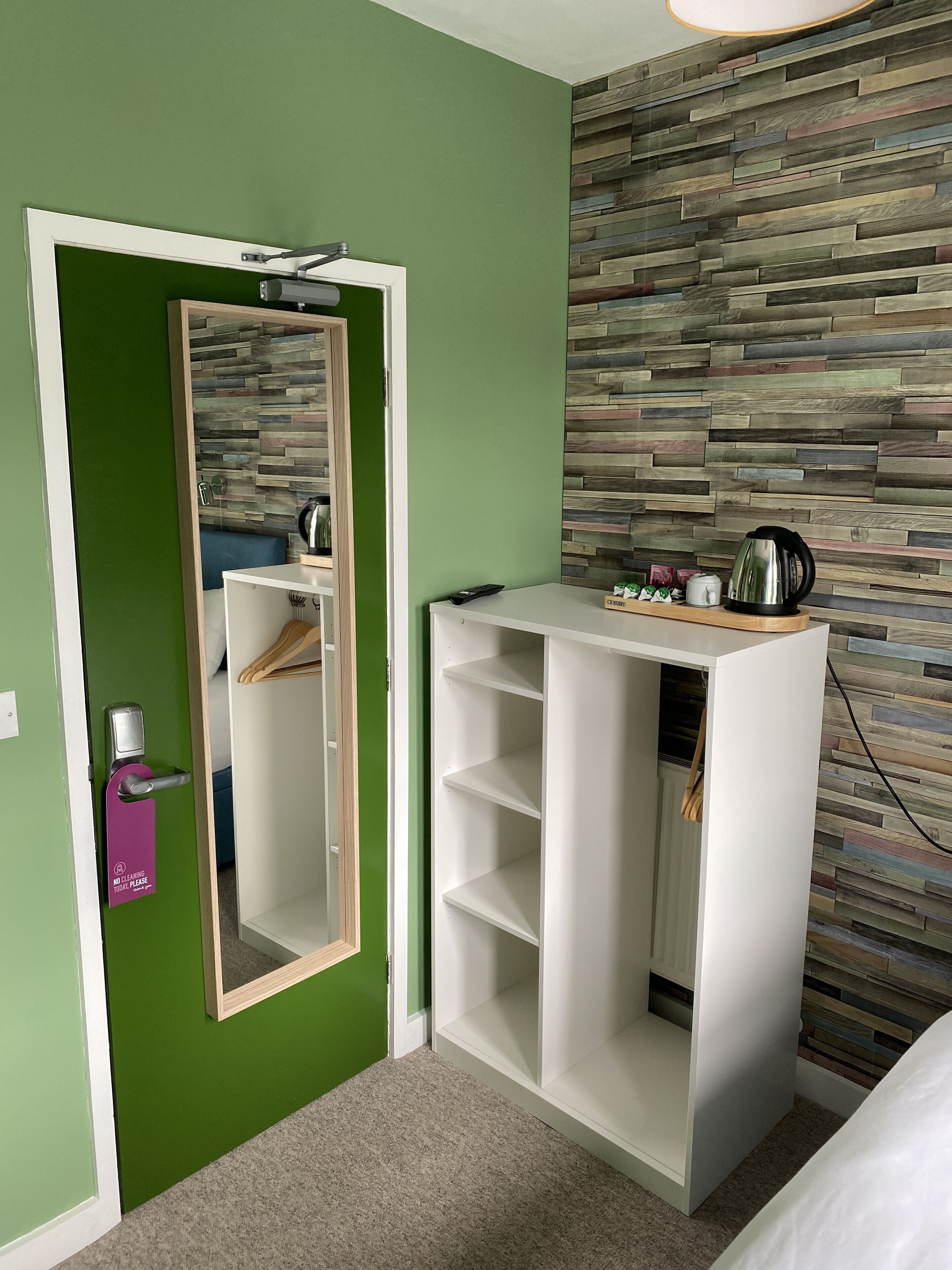 Een kamer met een groene wand, een paneel van houtstructuur, een witte garderobe met planken, en een spiegel.
