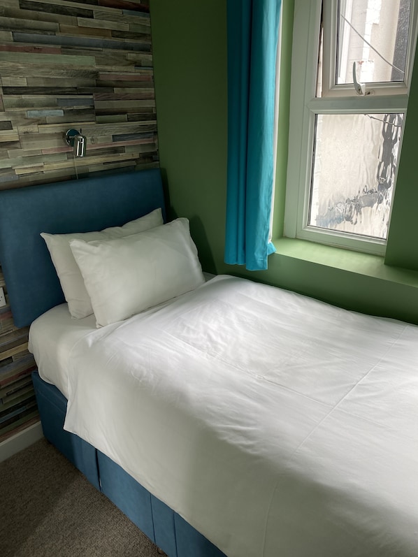 A neatly made bed with white linens, a blue headboard, and a wooden wall panel behind it. - WiseStay (Cardiff)