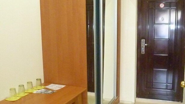 Une pièce comprenant une table à manger en bois, quatre chaises, une porte-fenêtre coulissante et une porte en bois foncé.