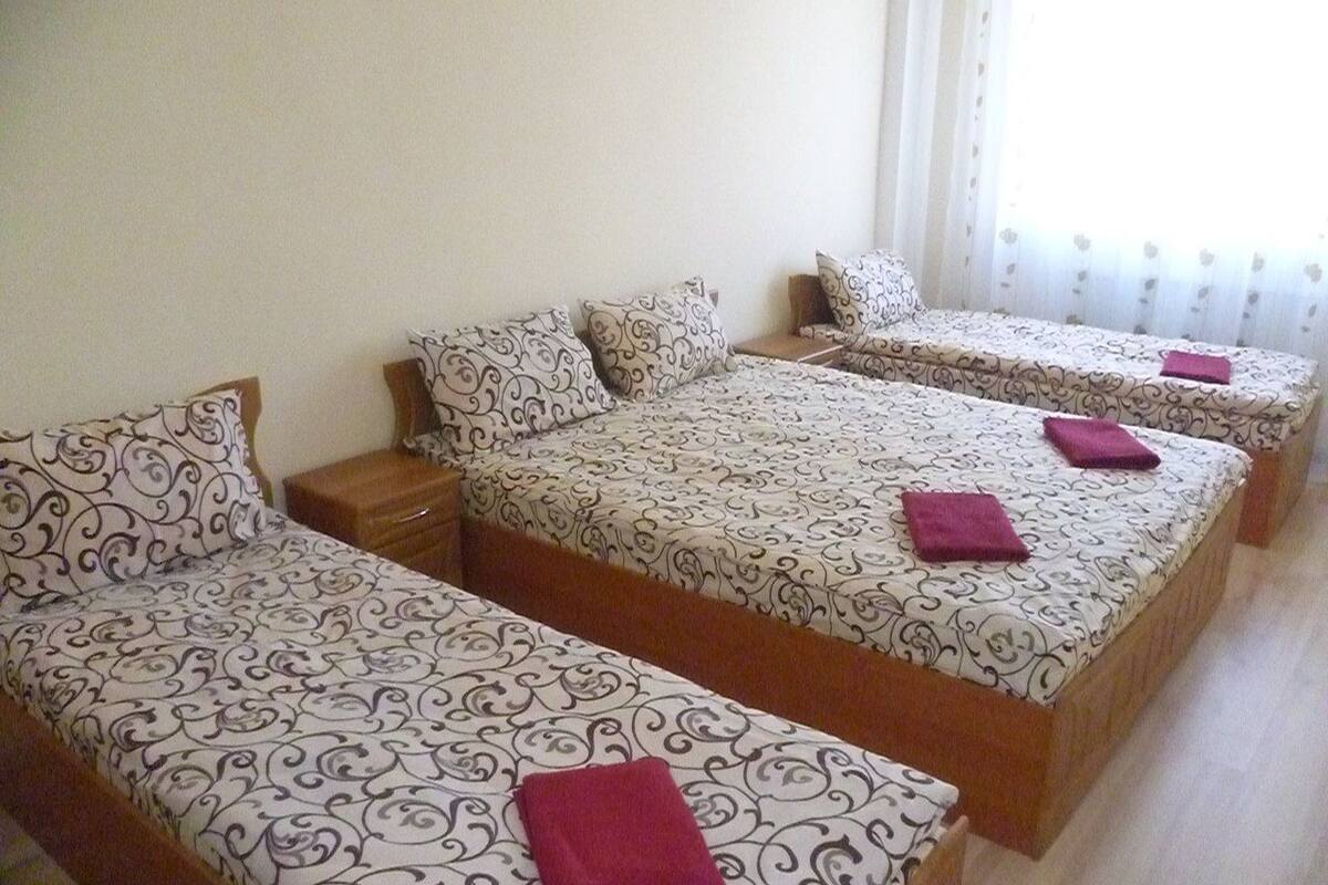 A hotel room with three single beds, each with a patterned bedspread and pillows.