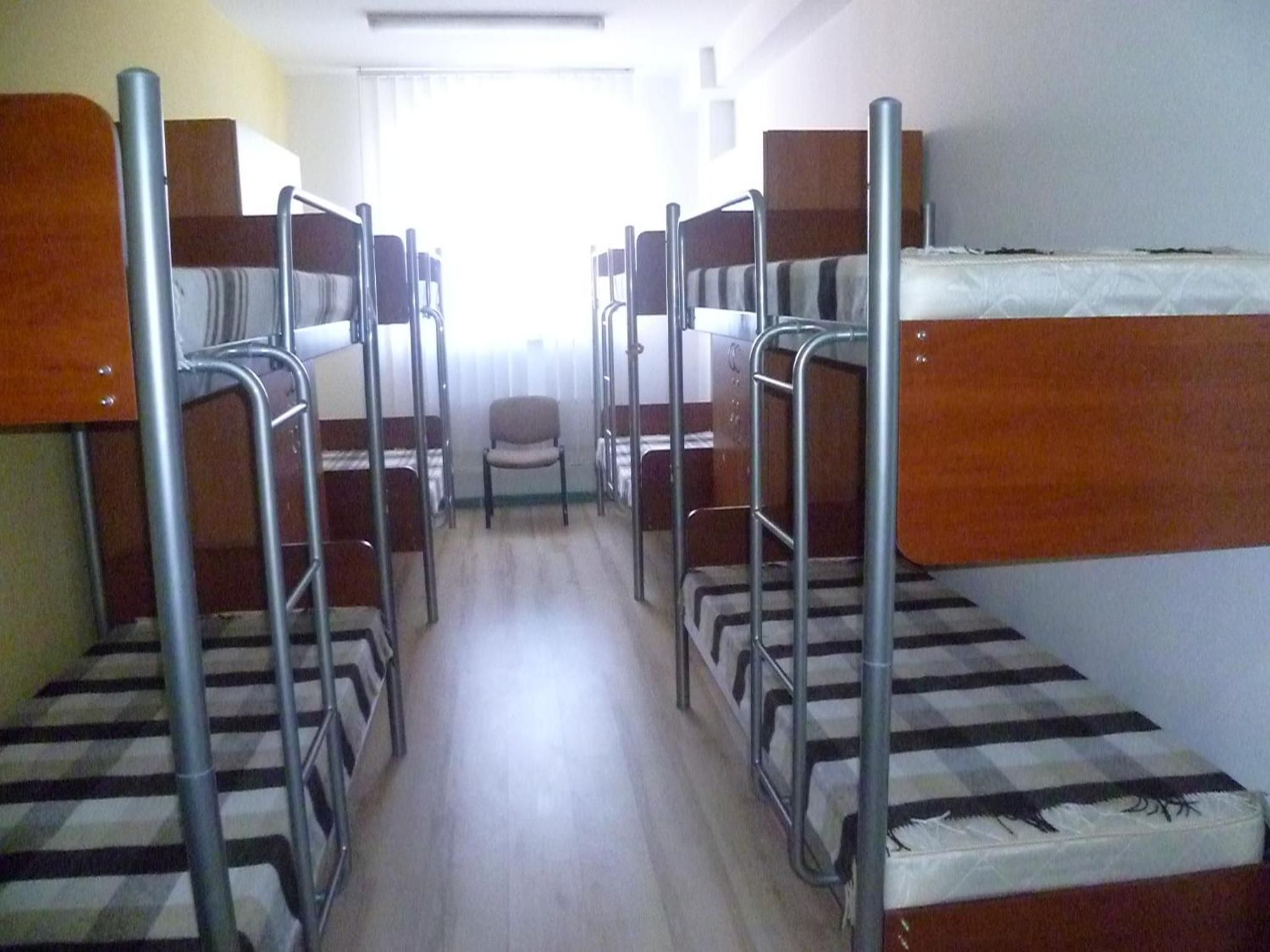 A corridor with bunk beds on either side, a chair in the center, and a window at the end.