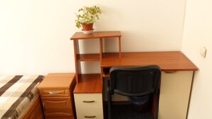 Une petite pièce, de taille modeste, comprenant un bureau en bois, une chaise, un petit meuble et une plante en pot.