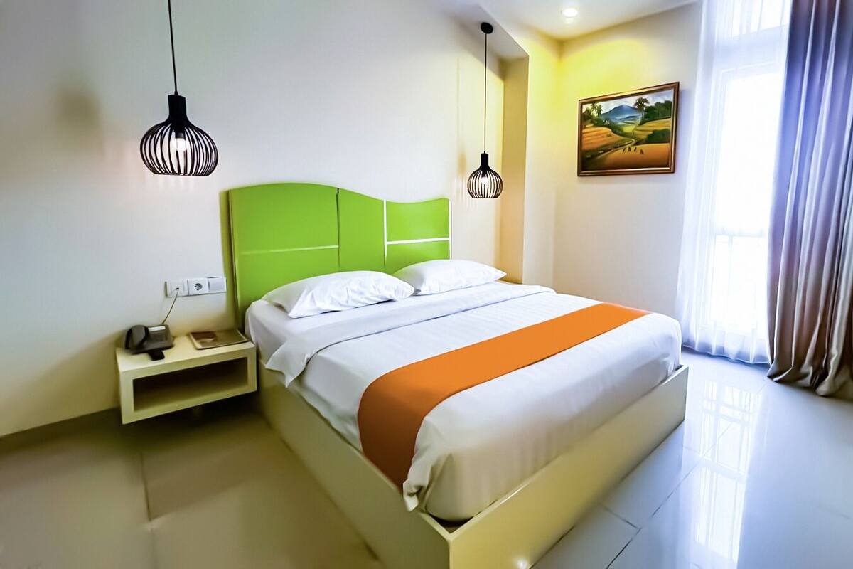 Een hotelkamer met een bed, nachtkastje, lamp en een schilderij aan de muur.