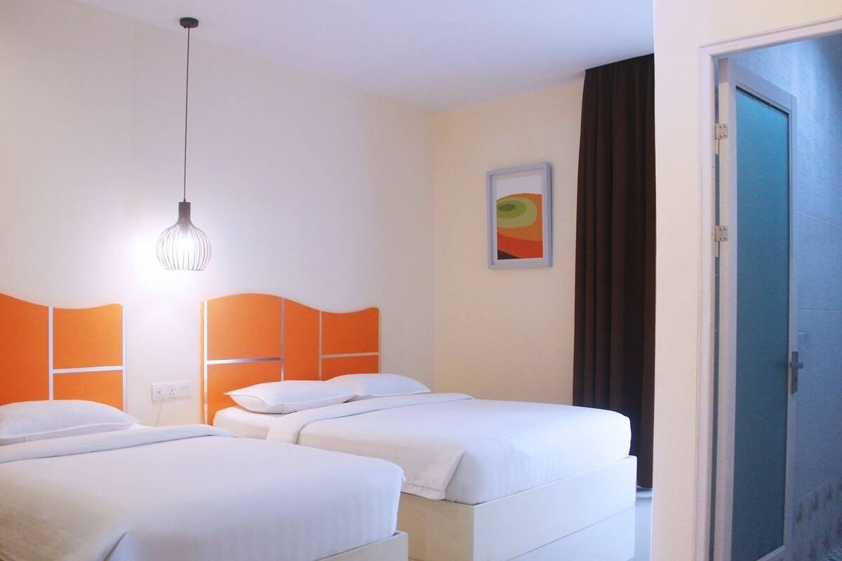 Een hotelkamer met twee bedden, één hanglamp en een deur naar een balkon.
