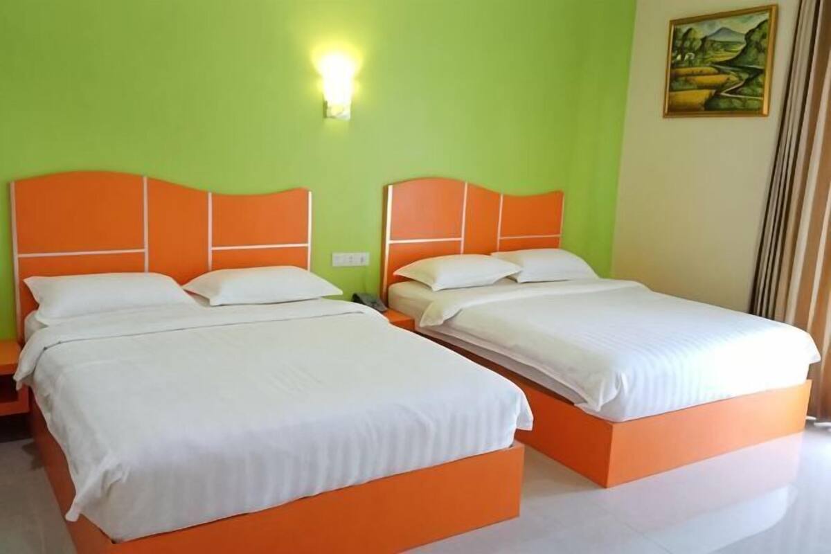 Een kamer met twee bedden, elk met een oranje hoofdbord en witte beddengoed, tegen een groene muur met een schilderij en een wandlamp.