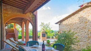 Un área de comedor al aire libre con una mesa lista para dos personas, rodeada de muros de piedra y una pérgola de madera.