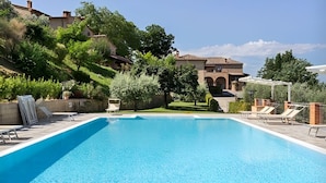 Una piscina rectangular con agua cristalina azul, rodeada de sillas de descanso y un jardín bien cuidado.