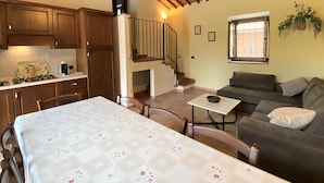 Una sala de estar acogedora con un sofá, una mesa de comedor con sillas, una cocina con armarios de madera y una escalera que sube a un nivel superior.